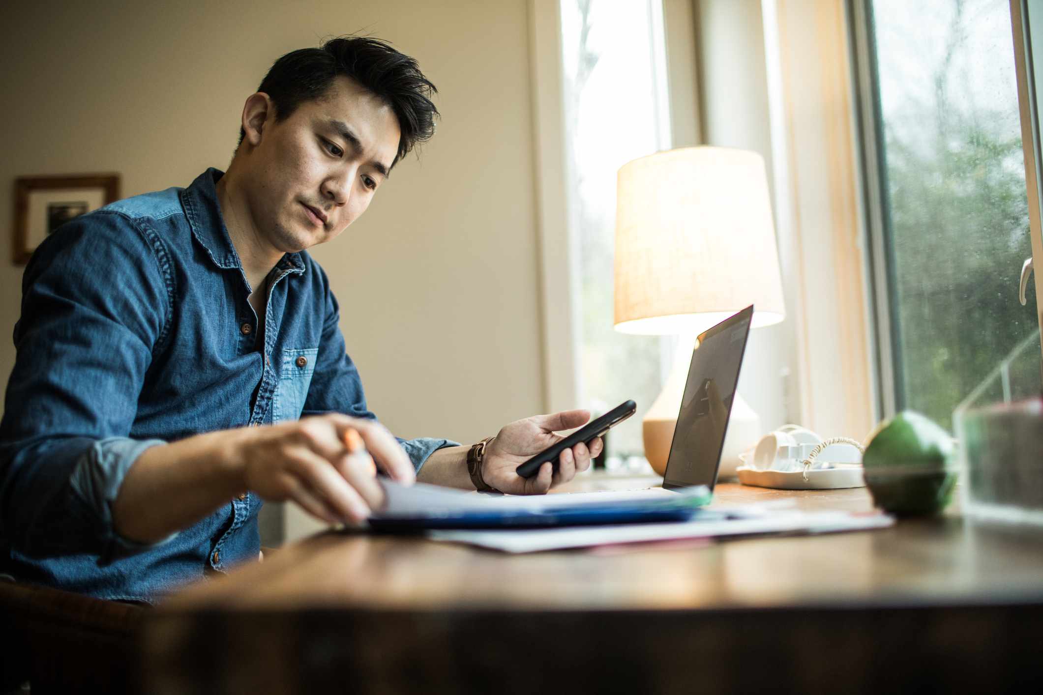 Seated man adds up Roth IRA savings with calculator and laptop