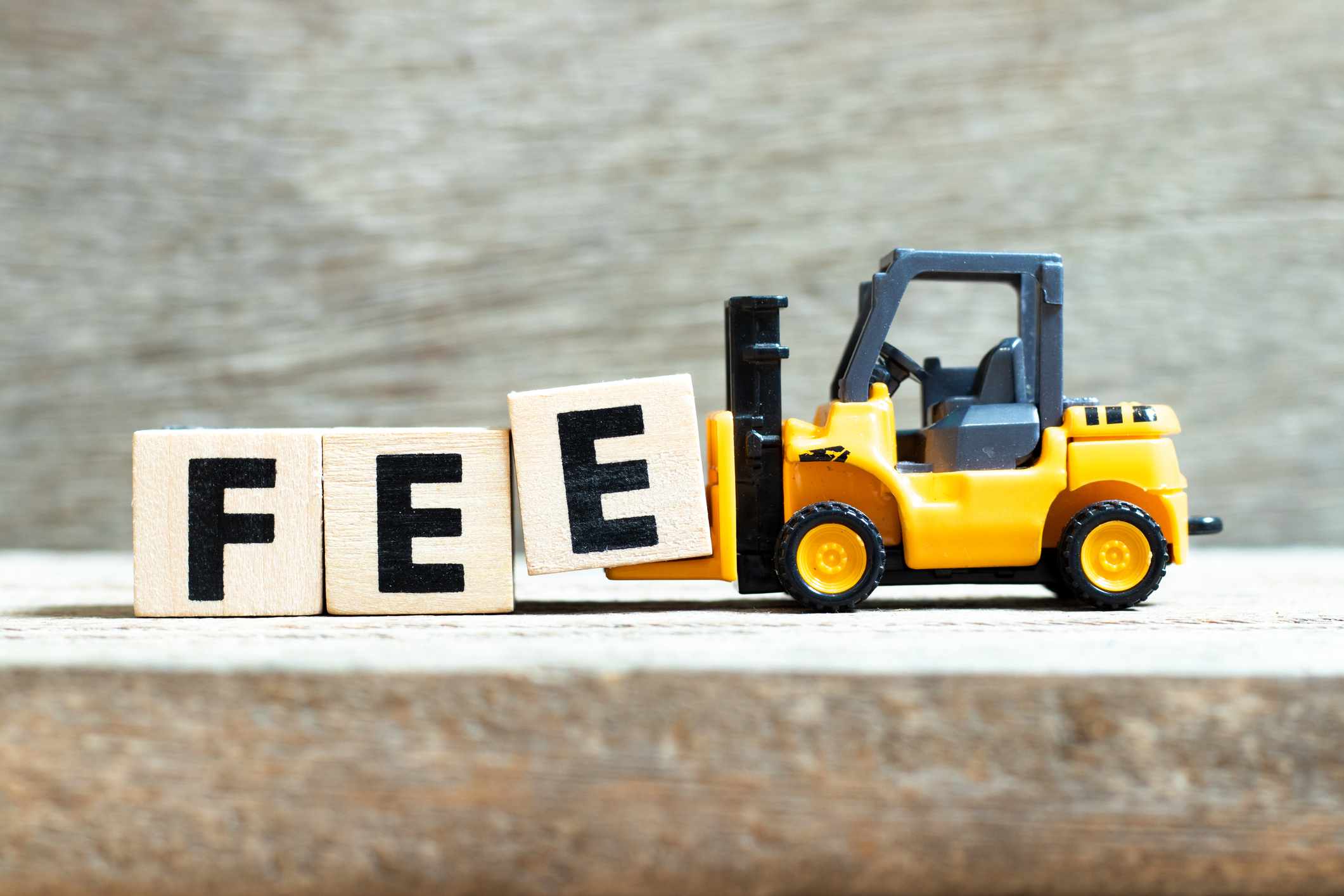 Toy forklift hold letter block e to complete word fee on wood background