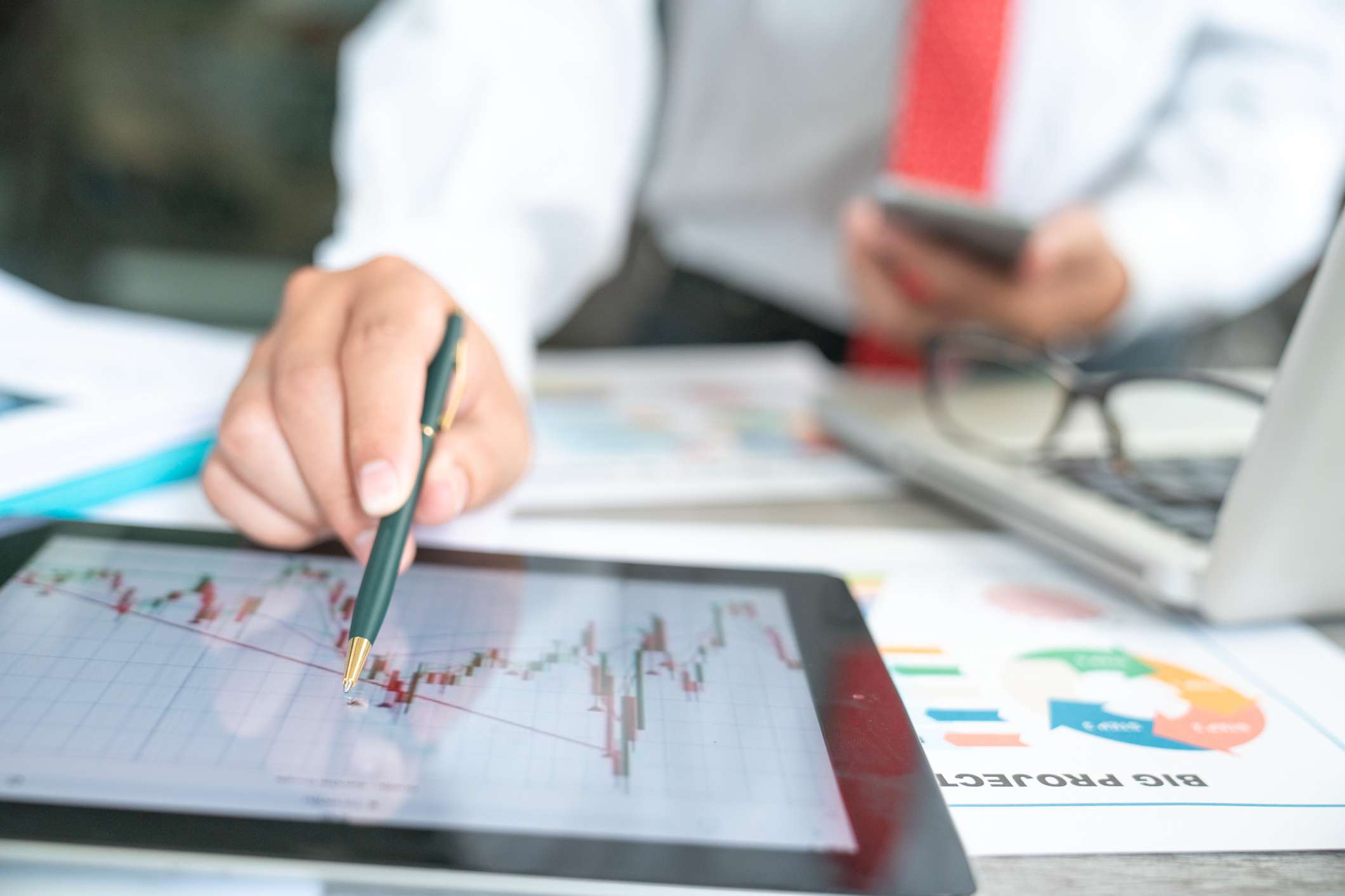 A man holding a pen pointing to a stock market chart on a tablet.