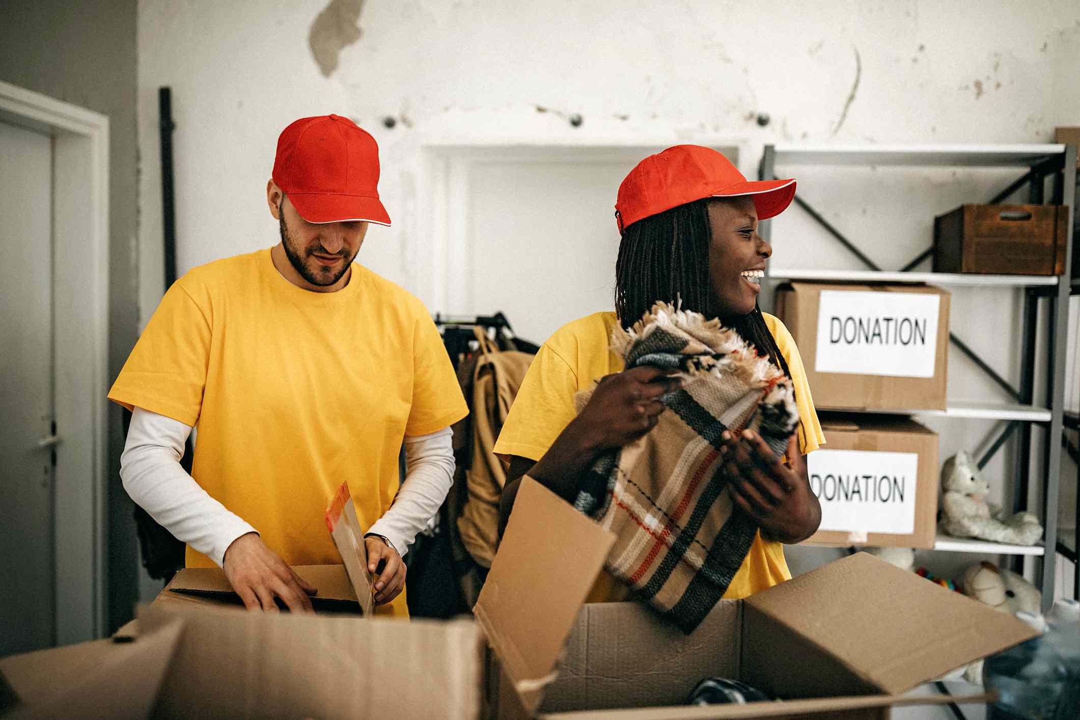 Man and woman in yellow t-shirts and red caps unboxing charity donations