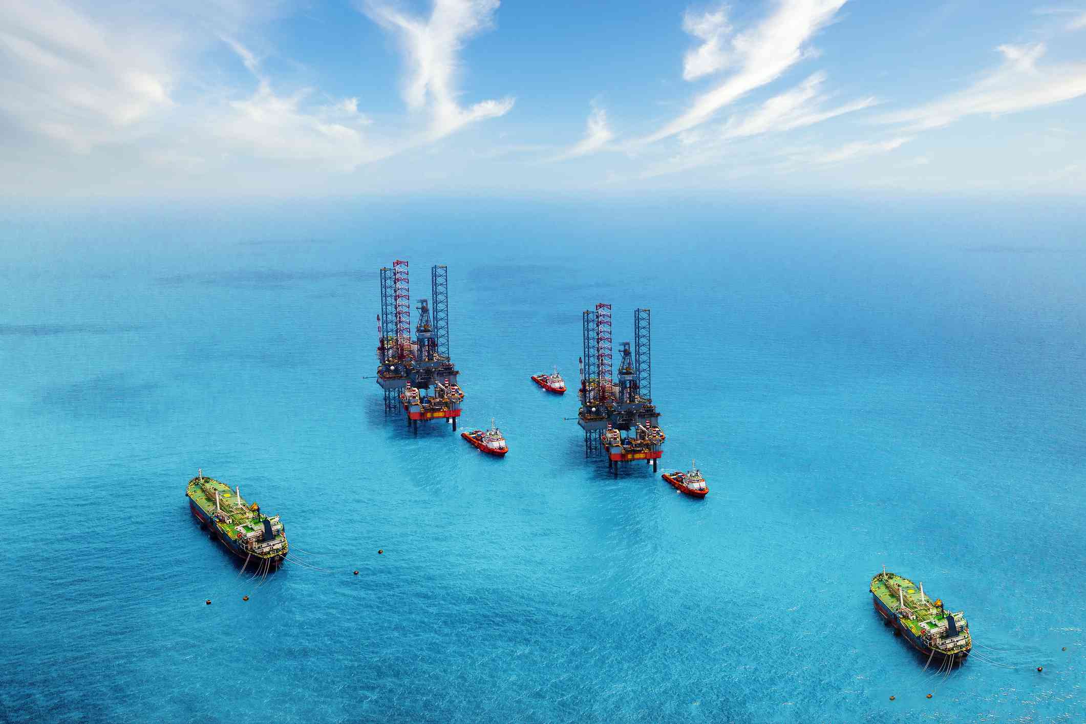 Aerial view of two oil rigs in the ocean surrounded by ships