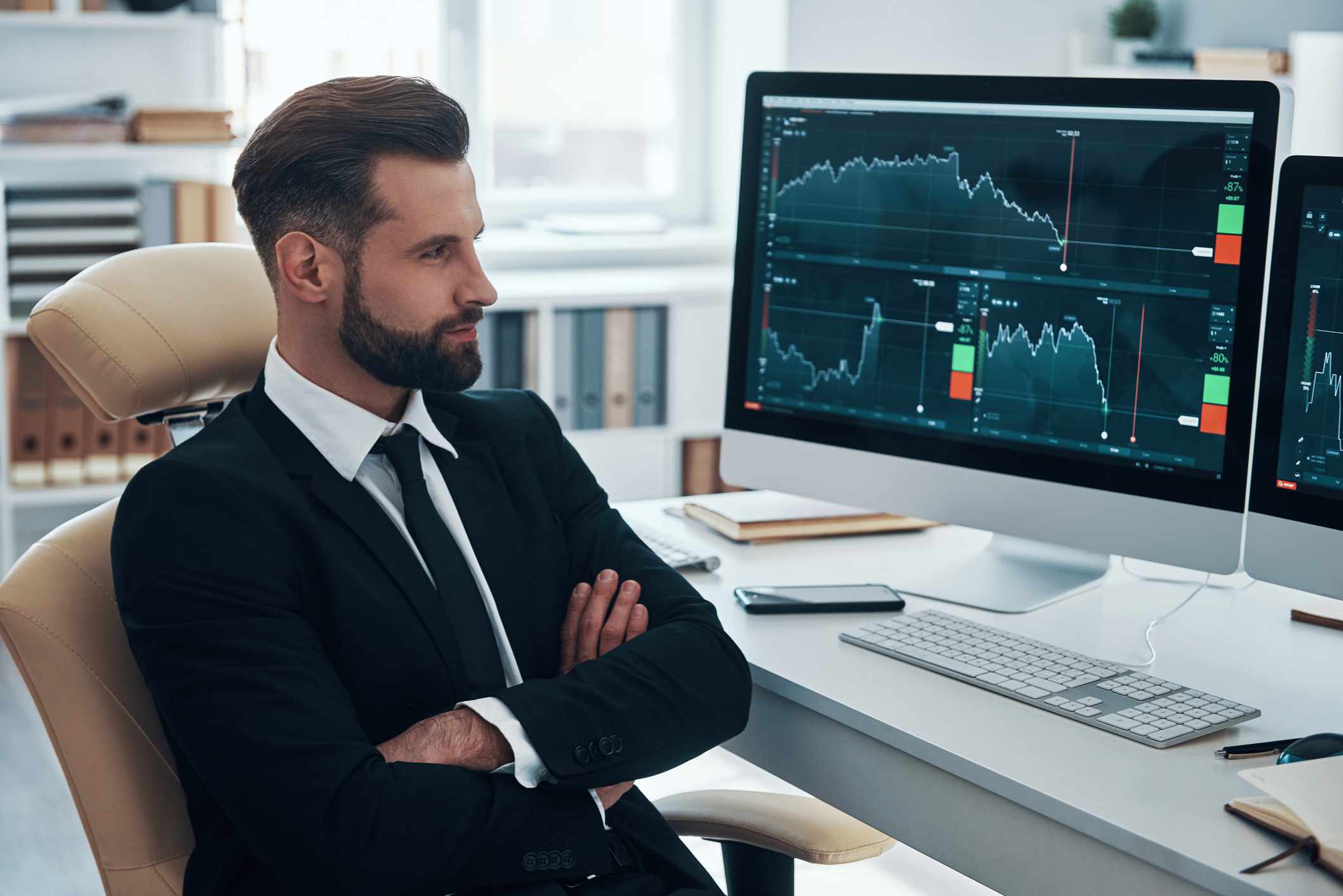Young business man in suit looking at financial charts on computer monitor
