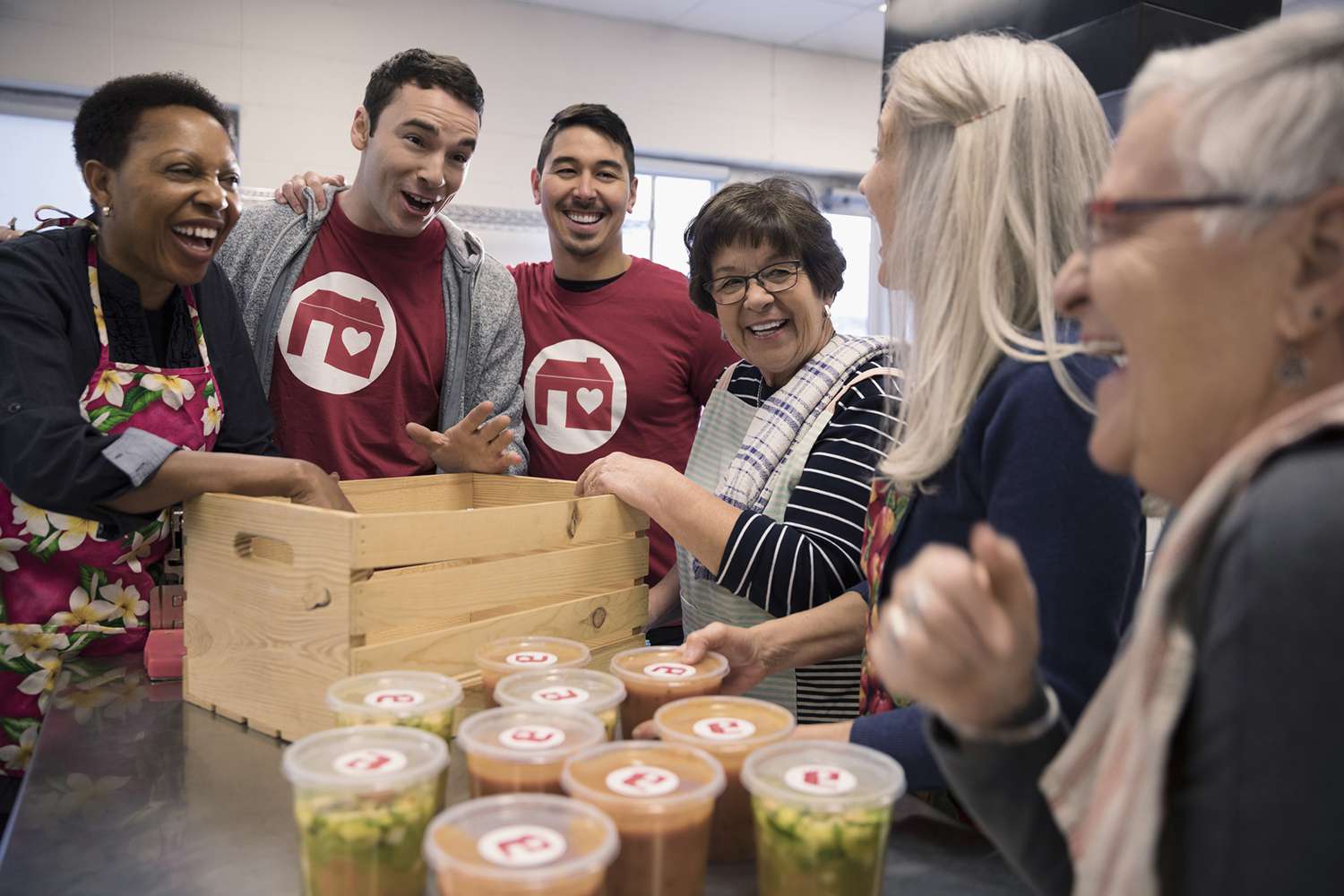 Playful Volunteers Packing Soup Containers in Crate in Soup Kitchen