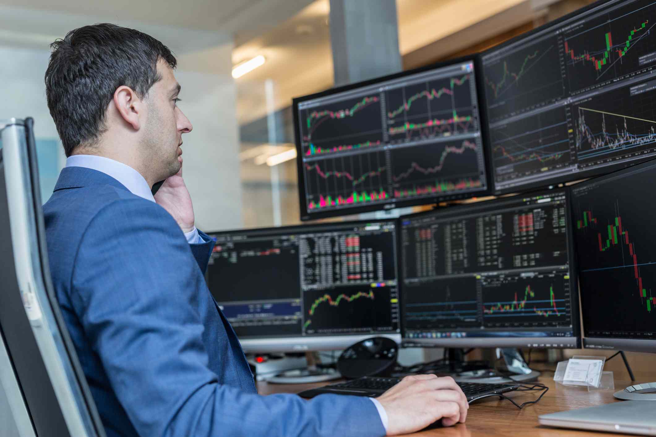 Stock broker trading online watching charts and data analyses on multiple computer screens.