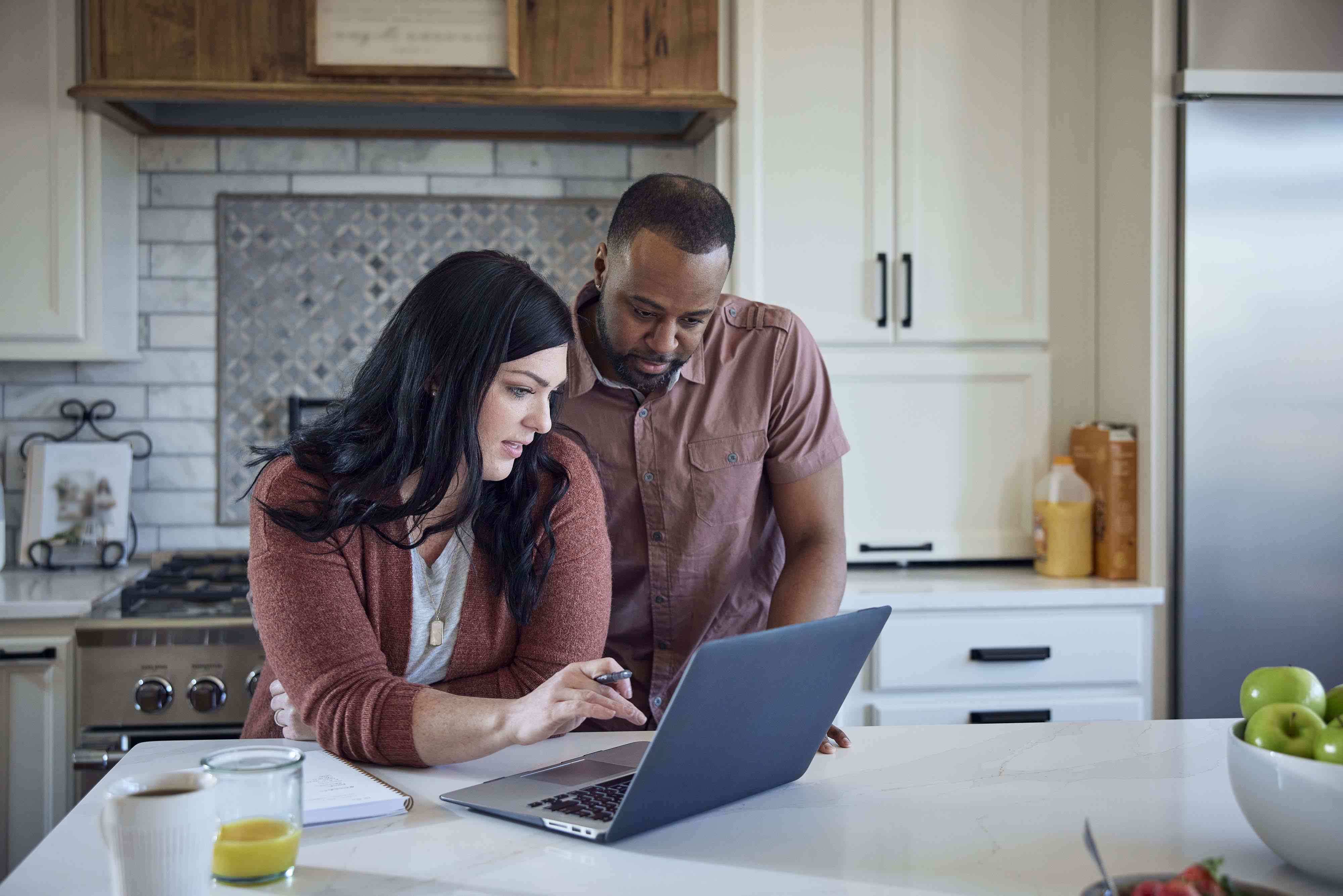 woman and man sit at kitchen counter working on laptop